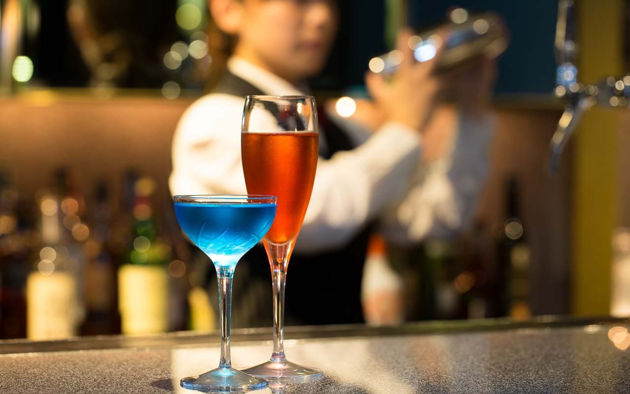 カウンターでシェイカーを振るバーテンダーとカウンターには美しいカクテル